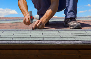 roofer hammering nail into asphalt roof shingle