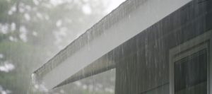 Rainwater pours off the edge of a roof during a heavy downpour, illustrating potential causes of roof leaks